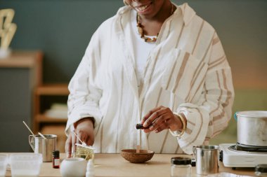 Masada duran bir kadın sıcak bir mutfak ortamında malzemeleri karıştırıyor, sıcak bir şekilde gülümsüyor. Çeşitli aletler kullanarak doğal ya da ev yapımı bir yemek tarifi hazırlamakla meşgul.