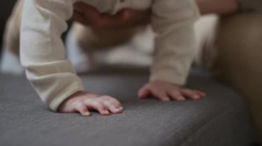 Gri kanepede oturan ve aktif bebeği destekleyen, düşmesini ve yaralanmasını önleyen, tanınamayan genç annenin yakın çekimleri.