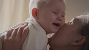 Beyaz bir kadının kucağında kucağında koşulsuz bir sevgiyle onu yanaklarından öptüğünü gösteren yüzü. Küçük çocuk sevgi dolu bir anneye sarılmak istiyor.