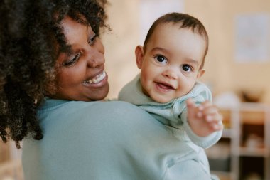 Afrikalı Amerikalı annesi ona sarılırken küçük çocuk elini kameraya çekiyor.
