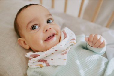 Büyük yuvarlak siyah gözlü, şirin bebek yüzlü orta boy, beşiğindeyken geniş bir gülümseme sergiliyor