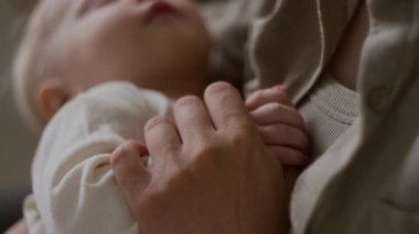 Elinde uyuyan bebeği tutan ve küçük bir ele dokunan, anne ve çocuk arasında derin bir bağ kuran tanınmamış genç bir kadının son derece yakın çekimi.