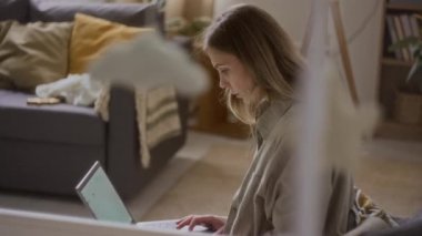 Orta boy beyaz bir kadın dizüstü bilgisayarla oturup beyaz karyolaya yakın bir salonda huzur içinde uyuyan tatlı bir bebekle çalışıyor.