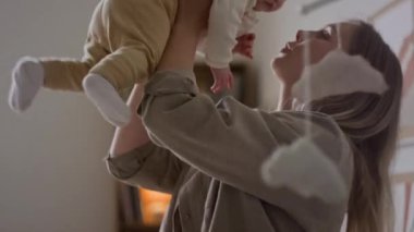 Orta boy beyaz bir kadının bebeği yatak odasında tutarken, yanağından öptüğü ve lüks bir gezginin dikkatini çektiği, küçük çocuğu keşif için cesaretlendirdiği bir fotoğraf.