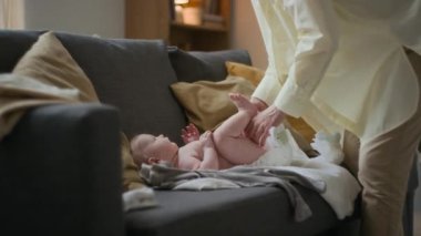 Orta kıvrımlı gülümseyen beyaz kadın günlük giysiler giyip bebek bezi değiştiriyor. Oturma odasında kanepede yatıyor. Dışarı çıkmadan önce.
