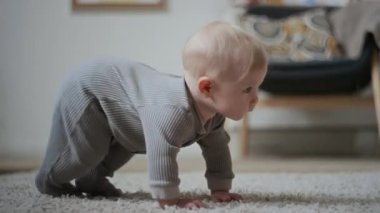 Gri halı zemininde sürünen sarı saçlı, sevimli beyaz bir bebek. Keşif odasına ve dünya ile etkileşime odaklanmış.