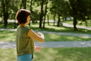 Yaz günü parkta meditasyon yapan tanınmayan yaşlı bir kadın. Etrafı kıymetli doğayla çevrili.