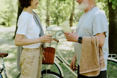 Yaşlı çift küçük bir mola verirken muhabbet ediyor ve su içiyor.