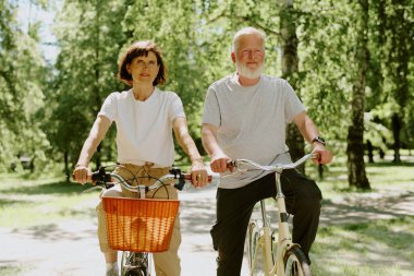 Yaşlı çift parkta bisiklet sürerken emekliliklerinin tadını çıkarıyor.