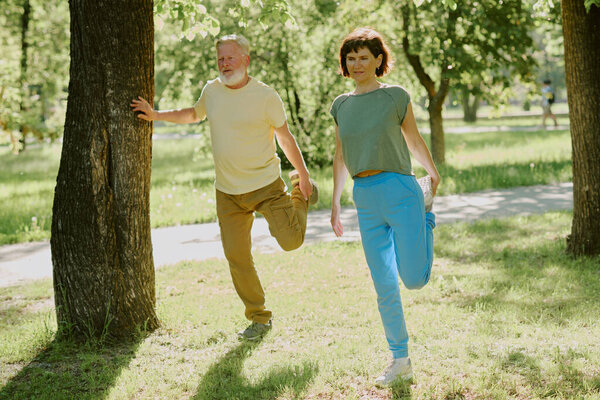 Senior couple stretching muscles and warming up joints in park during warm summer day