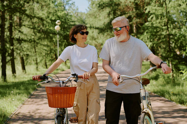 Прекрасный старший муж и его брюнетка жена гуляют с велосипедами в стиле ретро в парке