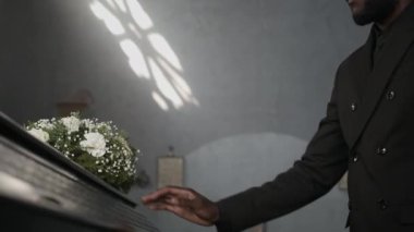 Siyah takım elbiseli Afro-Amerikan bir adam katedraldeki cenaze töreninde beyaz çiçeklerle elini tabut kapağının üzerinden uzatıyor.