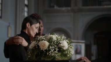 Siyahi kadın, kilisedeki anma töreninde onu teselli eden Kafkas kadın arkadaşının elini omzunda tutuyor.