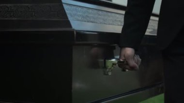 Siyah takım elbiseli, elinde tabutun sapı olan ve onu mezarlığa taşıyan tanınmamış bir gencin el görüntüsü.