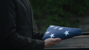 Açık hava anma töreninde, Amerikan bayrağını, üçgenden kadına katlayan tanınmayan bir adamın yakın çekim görüntüsü.