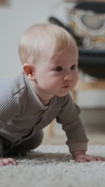 Sarışın, sevimli beyaz bir kız ya da erkek bebek halının dikey orta pozu. Halıda oturmuş merakla etrafı inceliyor.