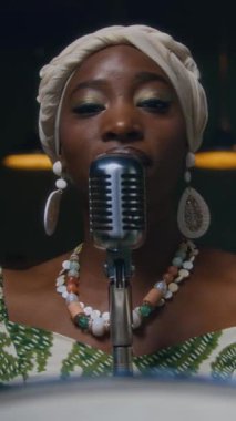 Siyahi kadın caz şarkıcısının müzik stüdyosunda mikrofonun önünde dikey görüntüsü.