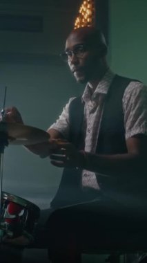 Afrikalı Amerikalı genç davulcunun müzik stüdyosunda enstrüman çalarken yüksek şapka ve zilleri kontrol ederken dikey çekimi.