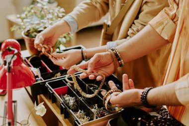 Mücevher dükkanında gösterilen kolye ve bilekliklerden seçilen ellerin yakın planında ayrıntılı ayrıntılar ve aksesuarlar dikkatlice incelenip seçiliyor.