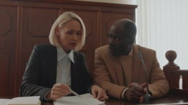 Beyaz kadın avukat, Afrikalı Amerikalı erkek müvekkiline davayı soruyor mikrofonu eliyle kapatıyor ve mahkeme salonunda ona cevap veriyor.