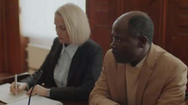 Asabi Afrikalı Amerikalı suçlayıcı davayı düşünüyor, sonra da düşüncelerini yanında oturan beyaz kadın savcıyla paylaşıyor.