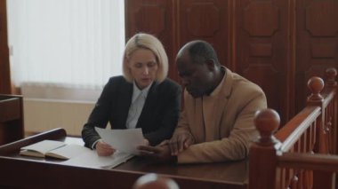 Kafkasyalı kadın savcı ve Afrikalı Amerikalı erkek davacı yasal belgelere bakıyor ve bunu mahkemede tartışıyorlar.