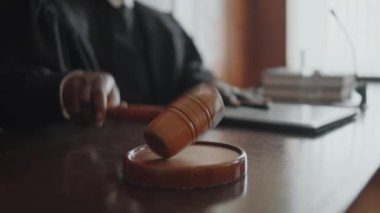 Tanımlanamayan bir yargıcın, duruşmanın başladığını duyururken tahta tokmakla ses bloğuna vurmasının yakın çekimi.