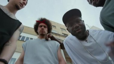 Sokakta dikilip kameraya özgüvenle poz veren dört cesur arkadaşın altında siyahi bir adam hip hop el hareketi yapıyor.