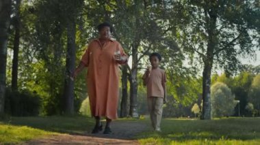 Afrikalı Amerikalı bir çocuğun, zengin parkında ya da ormanda boş bir yolda yürürken elinde kahve olan büyükannesiyle dondurma paylaşması.