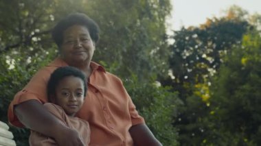 Afro-Amerikan büyükannenin portresi. Kısa saçlı. Yeşiller parkında bankta oturuyor.