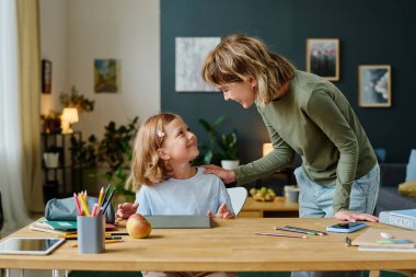 Sarışın anne, gündelik giysiler içinde masada oturup video oyunu oynarken küçük güzel kızını okşuyor.