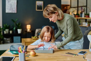 Genç anne ve kızı modern oturma odasında oyun oynuyorlar.