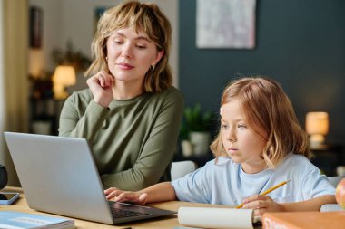 Annesi onu izlerken küçük kız masada oturup bilgisayar öğreniyor.