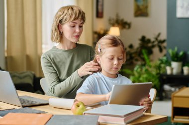 Genç anne tabletle çizgi film izlerken çocuğuna saç yapıyor.