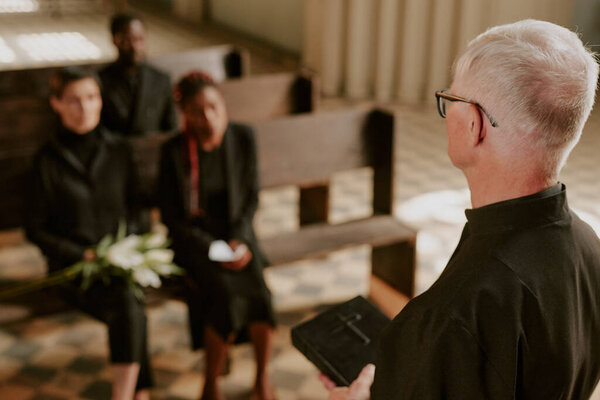 Over shoulder view of silver-haired priest offering up praying and holding Bible