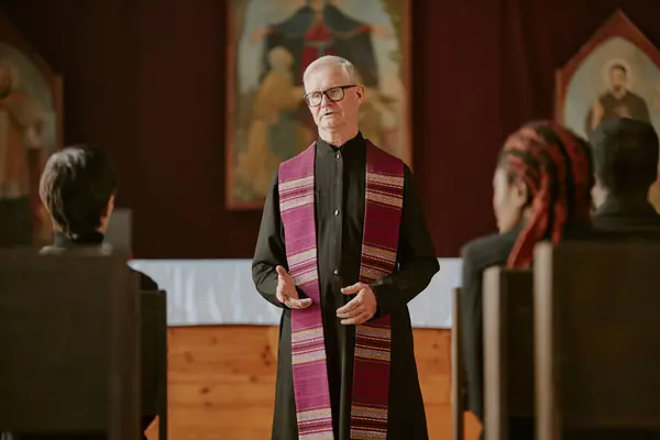 stock image Senior pastor offering up prayer while parishioners sitting on wooden bench and listening to it