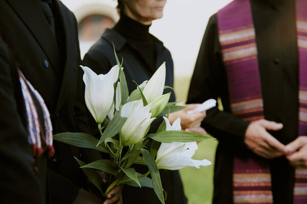 Unrecognizable hands holding bouquet of madonna lilies at funeral