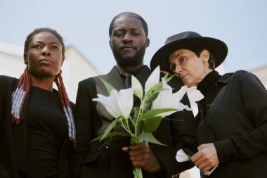 Anne Lily 'nin siyah giyinip kilise avlusundaki yas için ağladığı melez bir ailenin düşük açılı görüntüsü.