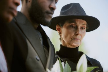 Kıdemli dul, çocuklarını ziyaret ediyor. Kocasının mezarı ve yanında beyaz buket getiriyor.