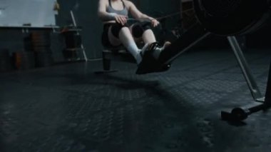 Spor kıyafetli genç bayan sporcunun spor salonundaki kürek çekme makinesinde vücut çalışmasını yakınlaştır.