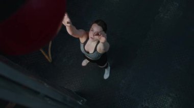 Spor salonunda spor yaparken duvar topu çömelmesi yapan güçlü genç bir kadının görüntüsü