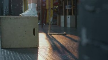 Beyaz çoraplı ve spor ayakkabılı, spor salonunda kutu atlayışı yapan tanınmayan bir kızın bacaklarının yan görüntüsü.