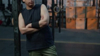 Çok ırklı bir gencin portresini büyüt. Kollarını kavuşturup halterlere yaslanmış spor salonundan sonra kameraya bakıyor.