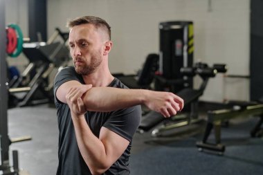 Ağır devre eğitiminden önce kollarını uzatan tonlu bir adam.