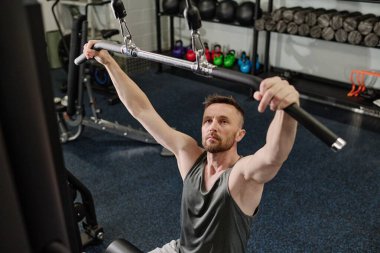 Adam bankta oturuyor ve ağırlık makinesini kullanmaya hazırlanıyor.