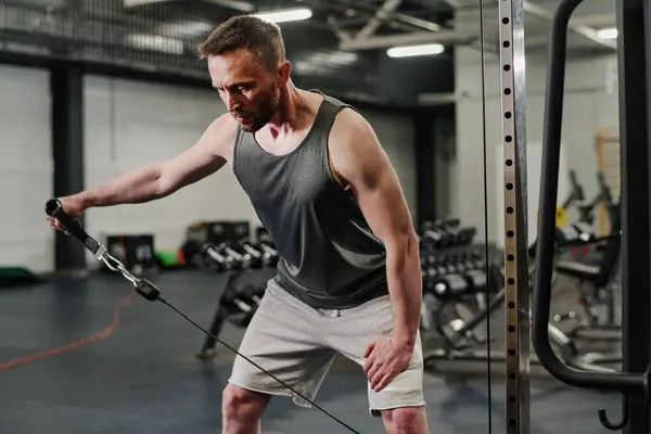 stock image Highly motivated professional coach pumping his shoulder with help of functional trainer in gym