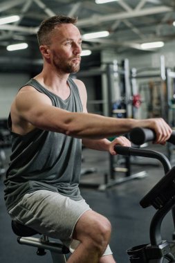 Sporcu adam popüler fitness kulübünde egzersiz bisikletinde kardiyo yapıyor.