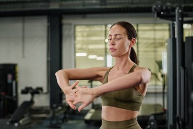 Genç, esmer, zeytin rengi giyinmiş kadın spor kıyafetleri giyip antrenmandan önce bileklerini ısıtıyor.