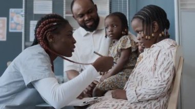 Afrika kökenli Amerikalı bir aile ve iki kızı klinikteki kadın çocuk doktorunu ziyaret ediyor. Saçlarını küçük bir kıza gösteriyor.