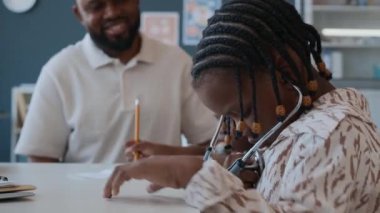 Babası ve kız kardeşiyle aile doktorunu ziyaret ederken steteskopla oynayan Afrikalı bir anaokulu öğrencisi.